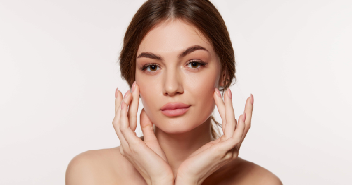 Young woman with flawless, dewy skin after SKINVIVE Treatment gently touching her face with both hands, showcasing a radiant complexion in Old Bridge, NJ.